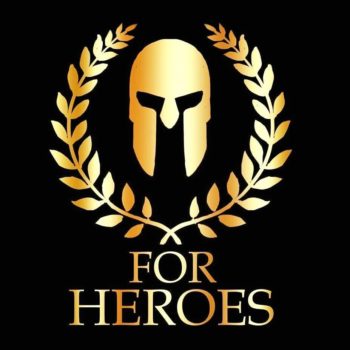 Logotyp Fundacji For Heroes. Logotyp ma kształt kwadratu, który jest czarnym tłem. Pierwszy plan zajmuje złota przyłbica a otacza ją wianek ze złotych liści. Pod spodem widnieje złoty napis For Heroes. Całość nawiązuje do motwu gladiatorów. 