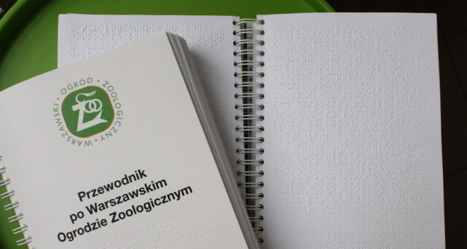 na zdjęciu widoczna jest książka zapisana językiem Braille'a. To jest przewodnik po warszawskim ogrodzie zoologicznym dla osób niewidomych i słabowidzących.