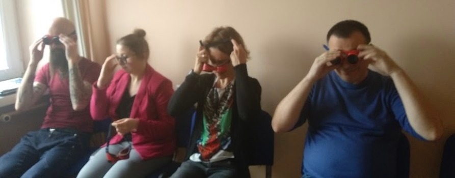 zdjęcie przedstawia grupę uśmiechniętych czterech osób, dwóch mężczyzn oraz dwie kobiety. Nakładają specjalne okulary, są wyraźnie tym zaciekawieni. Wszyscy siedzą. To szkolenie z audiodeskrypcji.