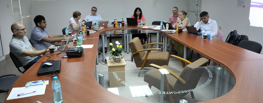 grupa uczestniczek i uczestników międzynarodowego projektu AWCAT podczas spotkania w Warnie, w Bułgarii. Wszyscy siedzą przy stole, a komputery stoją przed nimi.
