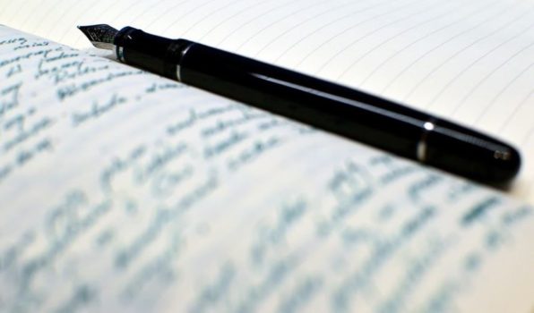 czarne pióro do pisania leżące na otwartym zapisanym notatniku