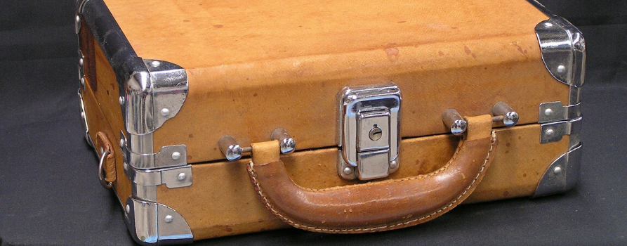 jasna skórzana walizka w stylu retro. walizka posiada metalowe srebrne zamknięcie oraz takie same metalowe okucia na rogach.
