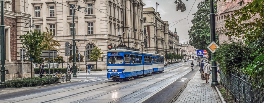 ulica Krakowa. po torach tramwajowych jedzie niebieski tramwaj, po chodniku idą przechodnie.