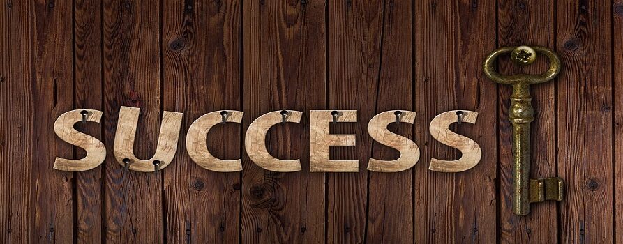 Grafika, przedstawiająca napis Success na drewnianych deskach. Obok napisu złoty klucz