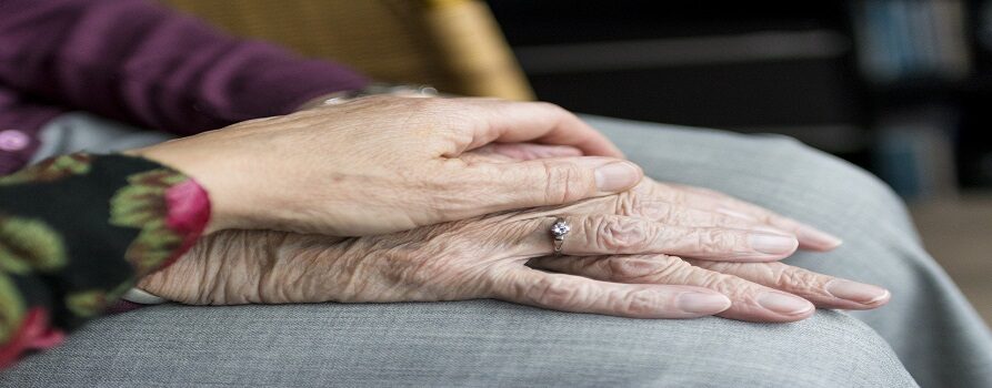 Ręka starszej osoby, na której w geście pomocy i przyjaźni spoczywa ręka osoby młodej