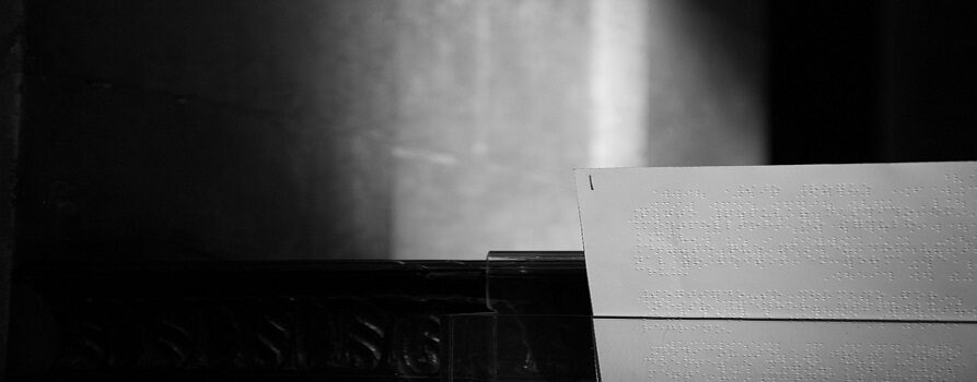 biała kartka, zapisana alfabetem Braille'a. W tle wnętrze prawdopodobnie starego kościoła