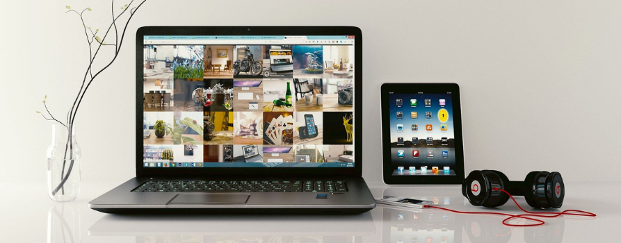 Otwarty laptop, na nim różne programy i aplikacje, obok słuchawki oraz tablet