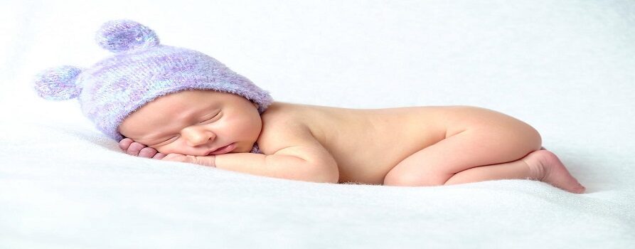 noworodek leżący na białej poduszce, w fioletowej czapeczce