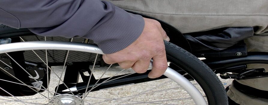 ręka mężczyzny, przesuwająca koło wózka inwalidzkiego