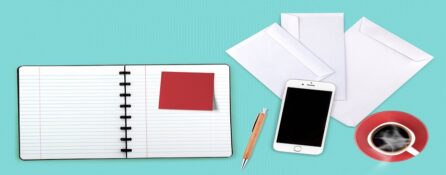 Rozłożony notatnik, na nim post-it, telefon komórkowy, filiżanka kawy, koperty