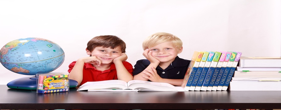 dwóch uczniów szkoły podstawowej, siedzą przy biurku w otoczeniu książek i pomocy naukowych, uśmiechają się